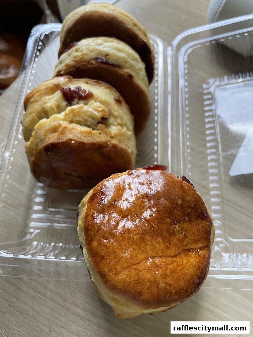 A close-up shot of freshly baked scones with visible fruit pieces inside, presented in a clear plastic container.