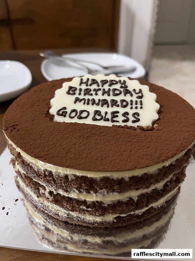 A layered chocolate cake with cream filling, dusted with cocoa powder and a personalized birthday message.