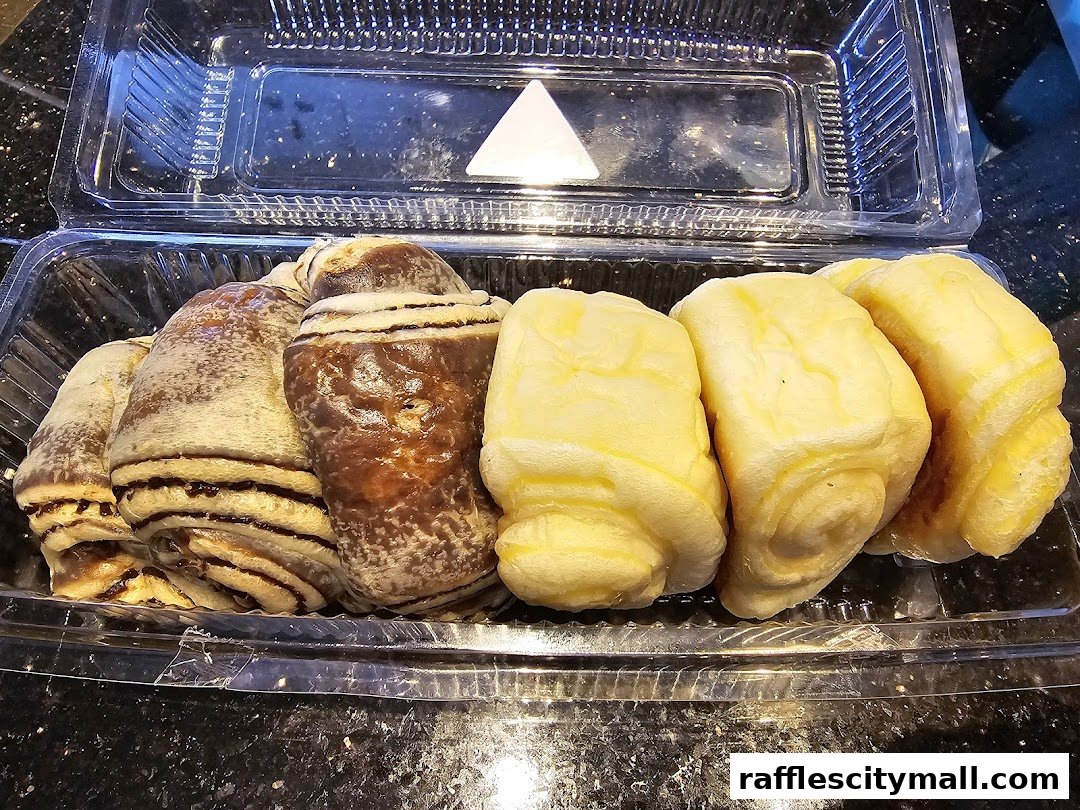 A clear plastic container filled with assorted pastries, including swirled chocolate and plain buns.