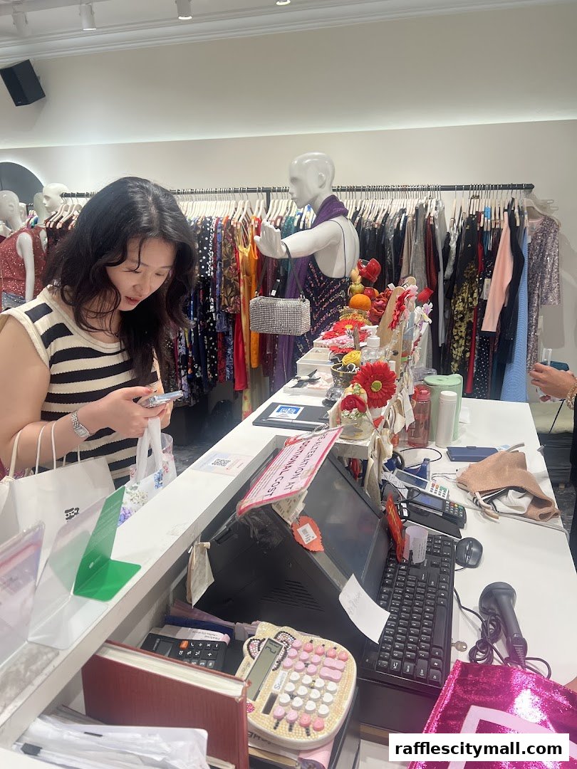 A woman is at the counter of a clothing store, looking at her phone.