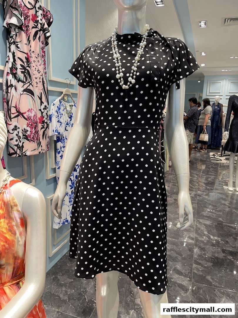 Mannequins display stylish dresses and pearl necklaces in a well-lit boutique.