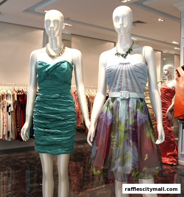 Two mannequins display stylish dresses and necklaces in a well-lit boutique.