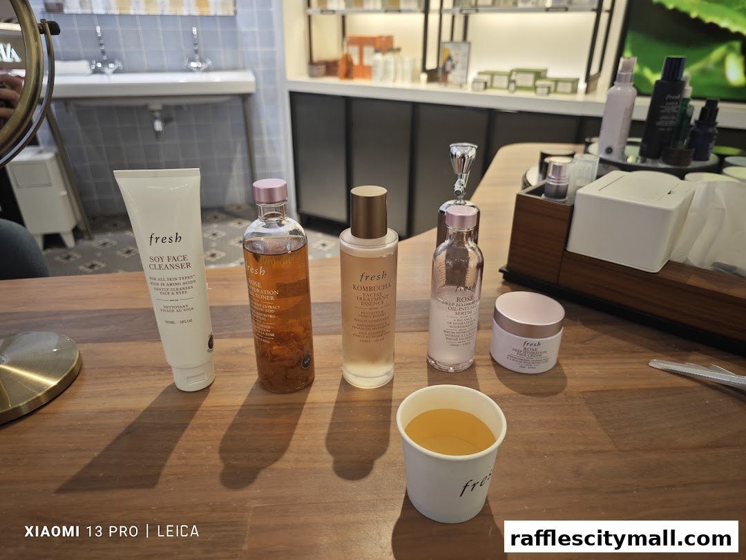 A collection of Fresh skincare products displayed on a wooden table with a cup of tea.