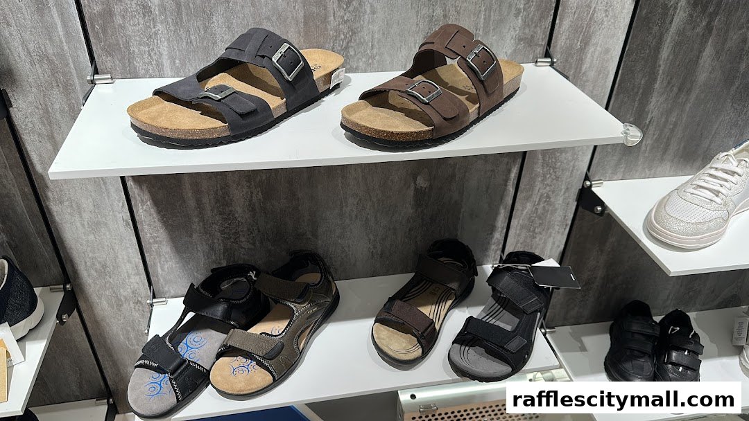 A display of various Geox sandals and sneakers on white shelves against a textured gray wall.