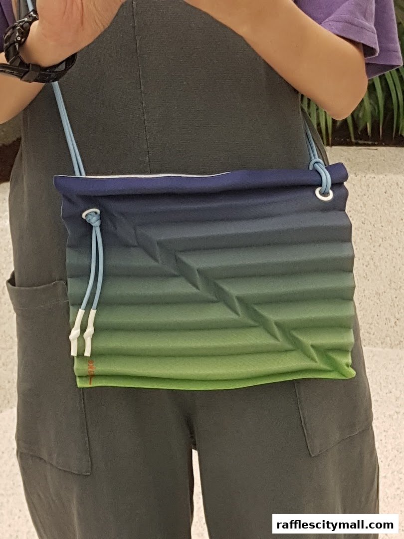 A person wearing a grey jumpsuit and holding a gradient blue and green crossbody bag.