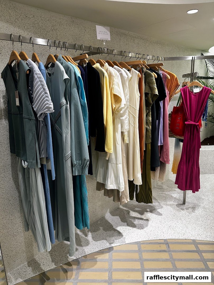 A rack of stylish, pleated clothing in various colors, including a bright pink dress.
