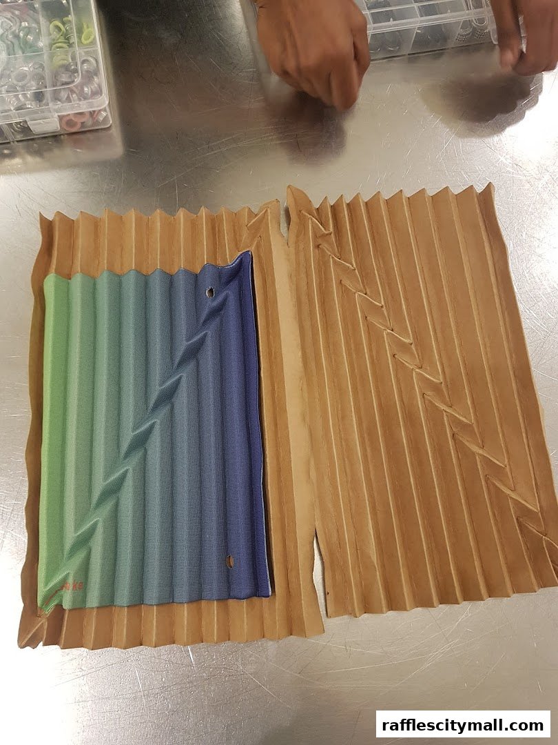 A close-up of a pleated fabric sample with a gradient of green to blue, next to a folded paper sample.