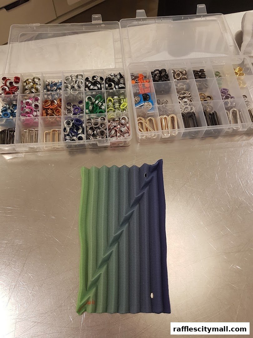 A collection of grommets and fasteners organized in a clear case next to a pleated fabric swatch.