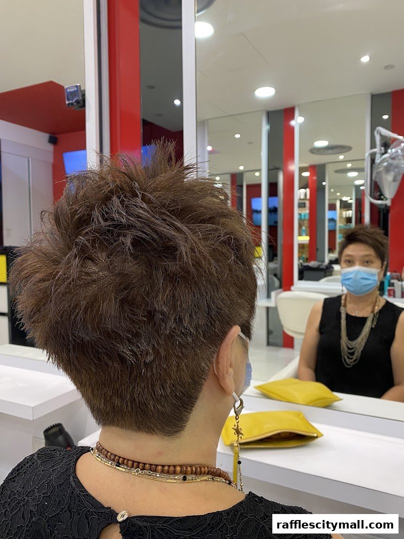A woman with a short, textured haircut sits in a salon, reflected in a mirror.