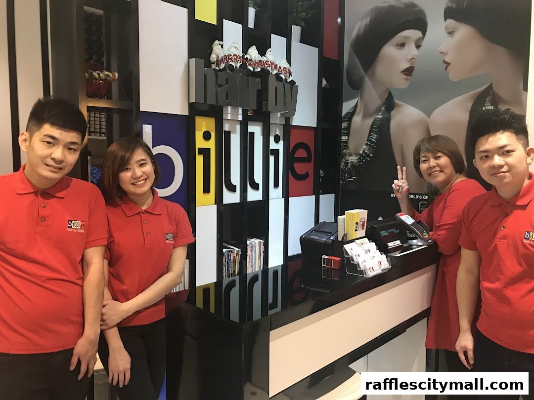 A team of smiling staff in red uniforms stand behind a reception desk at Hair by Billie.