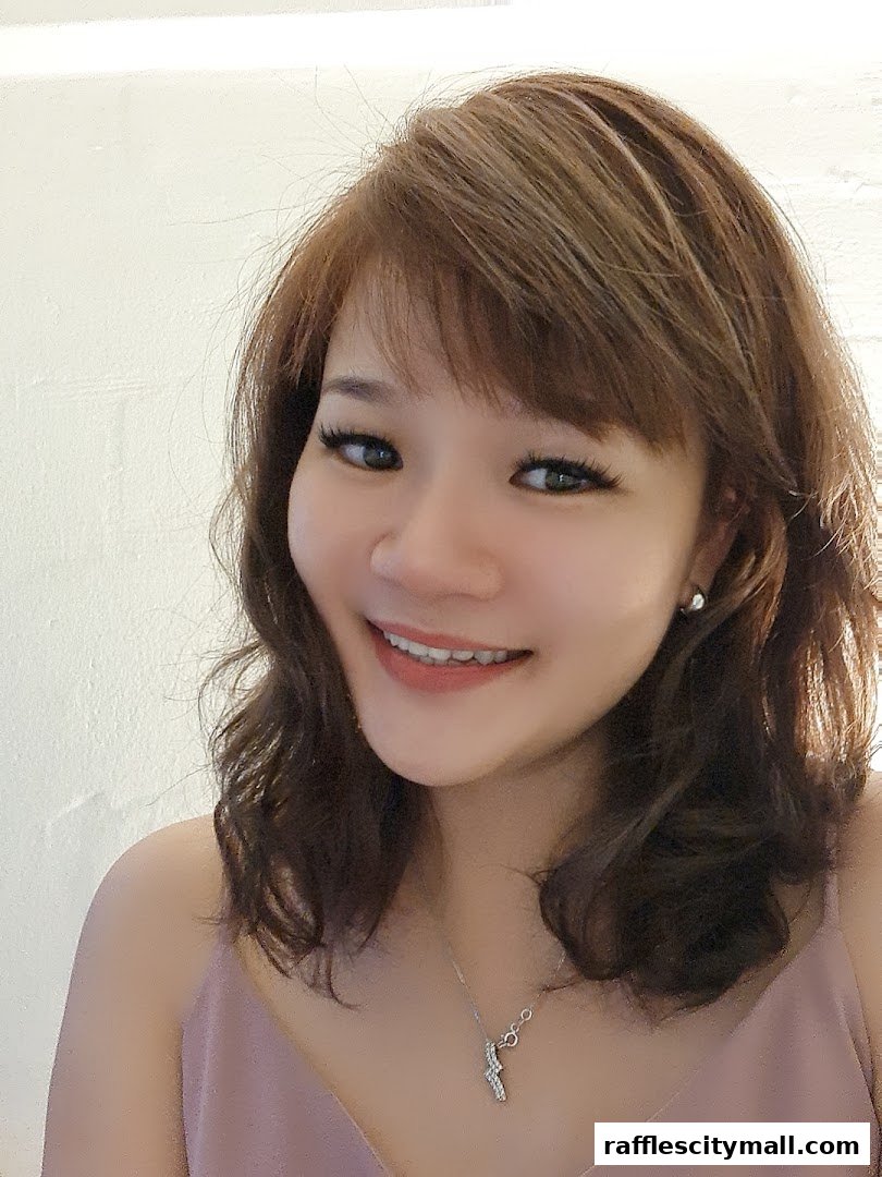 A smiling woman with brown hair and makeup, wearing a pink top and necklace.