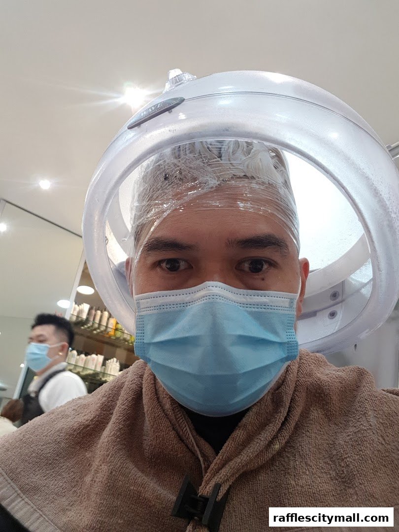 A person with a face mask under a hair steamer at a salon.