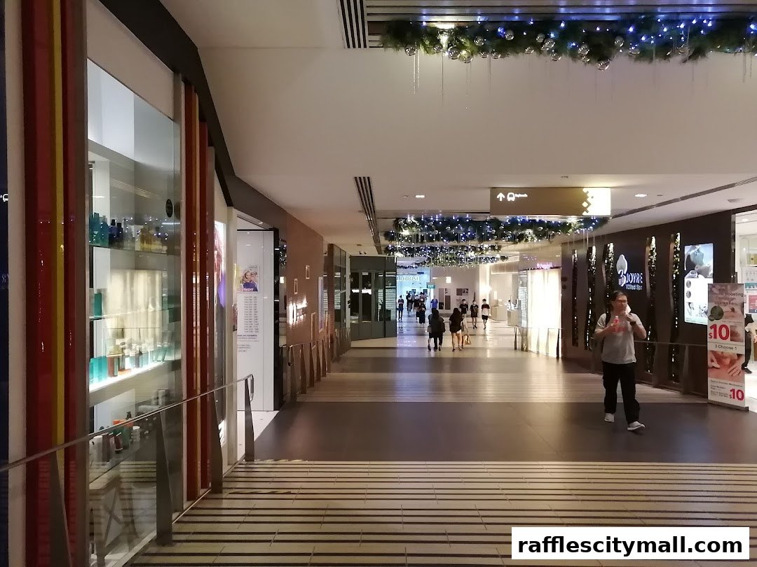 A shopping mall corridor with various shops and people walking.