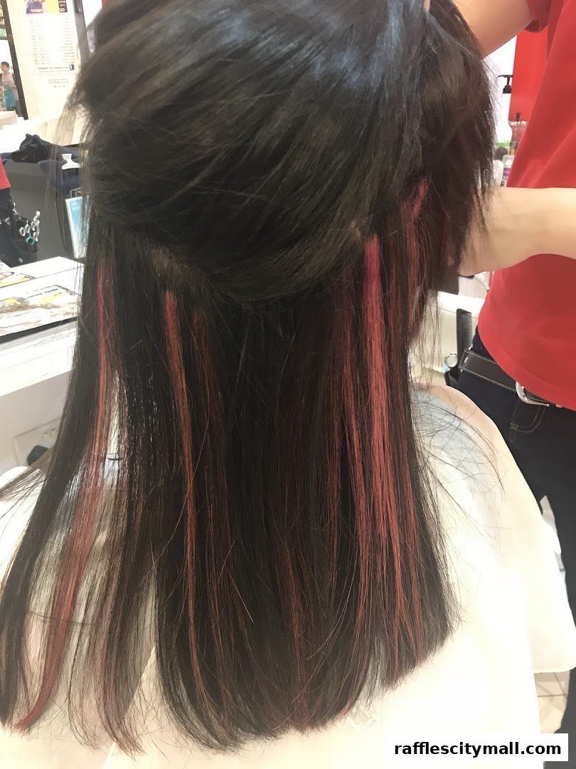 A person's dark hair with pink highlights being styled by a hairdresser.