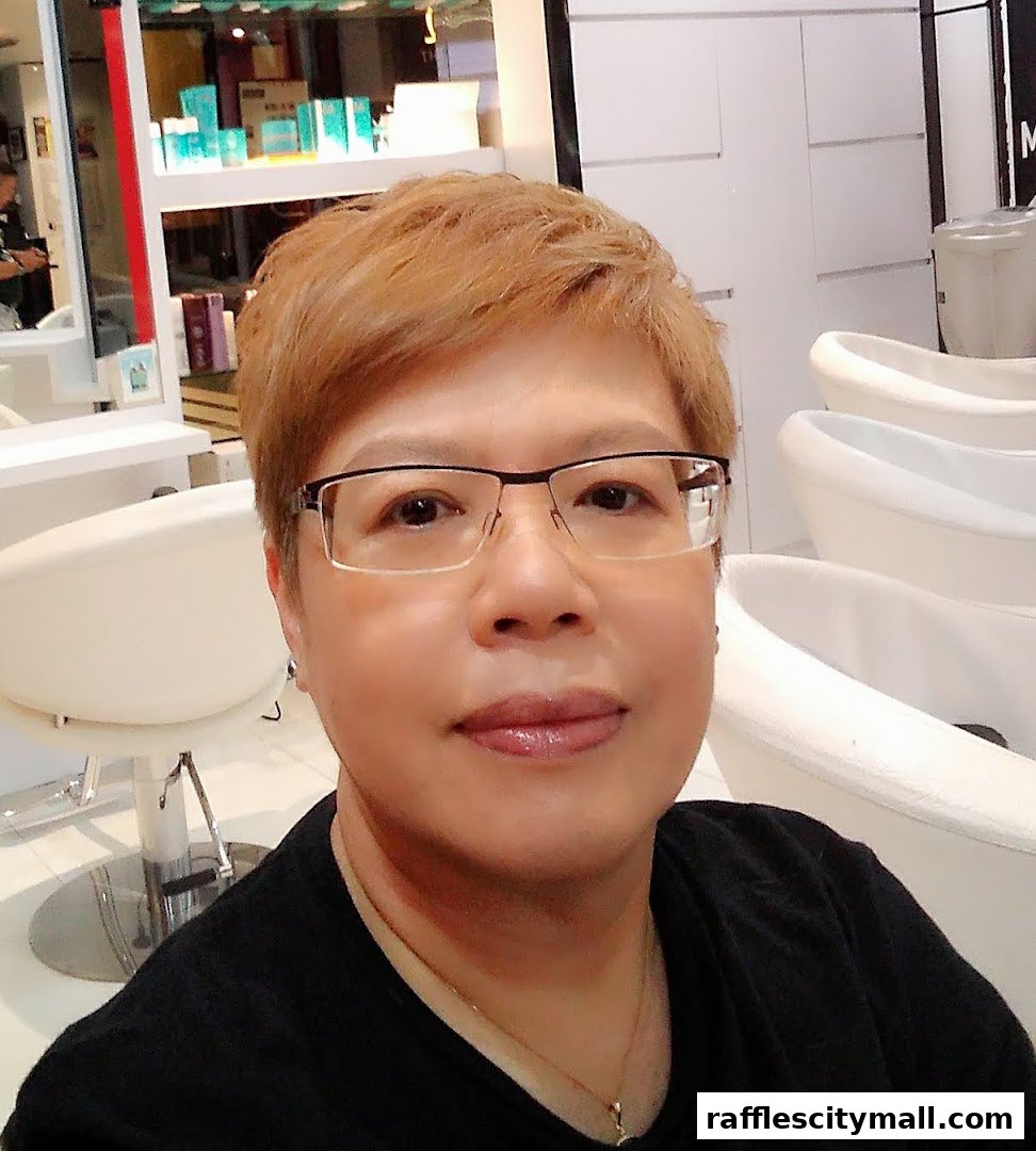 A person with short, reddish-brown hair and glasses smiles at the camera in a salon.