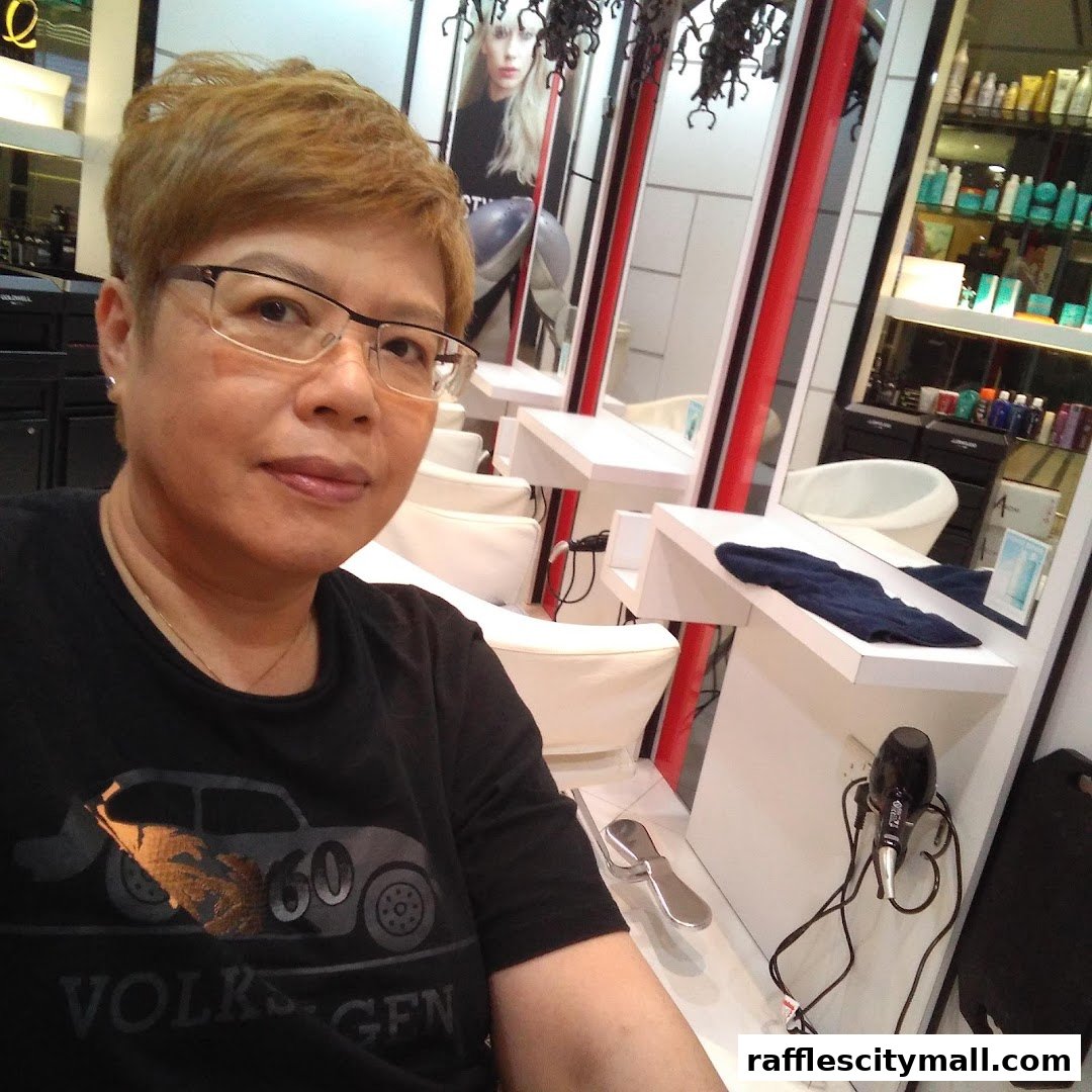 A woman with short, blonde hair and glasses takes a selfie in a modern hair salon.