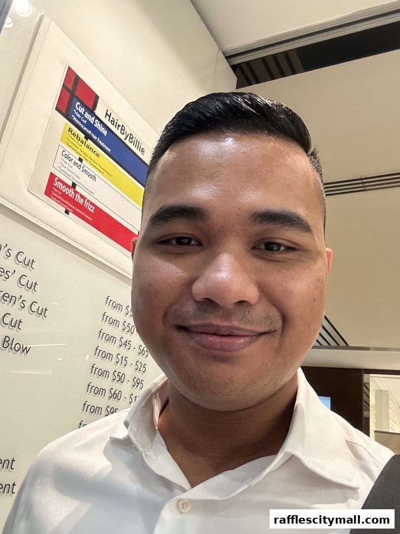 A man smiles at the camera in front of a price list for Hair by Billie services.
