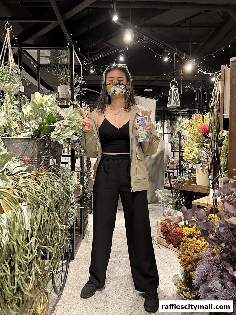 A person poses with peace signs in a shop filled with various plants and decor.