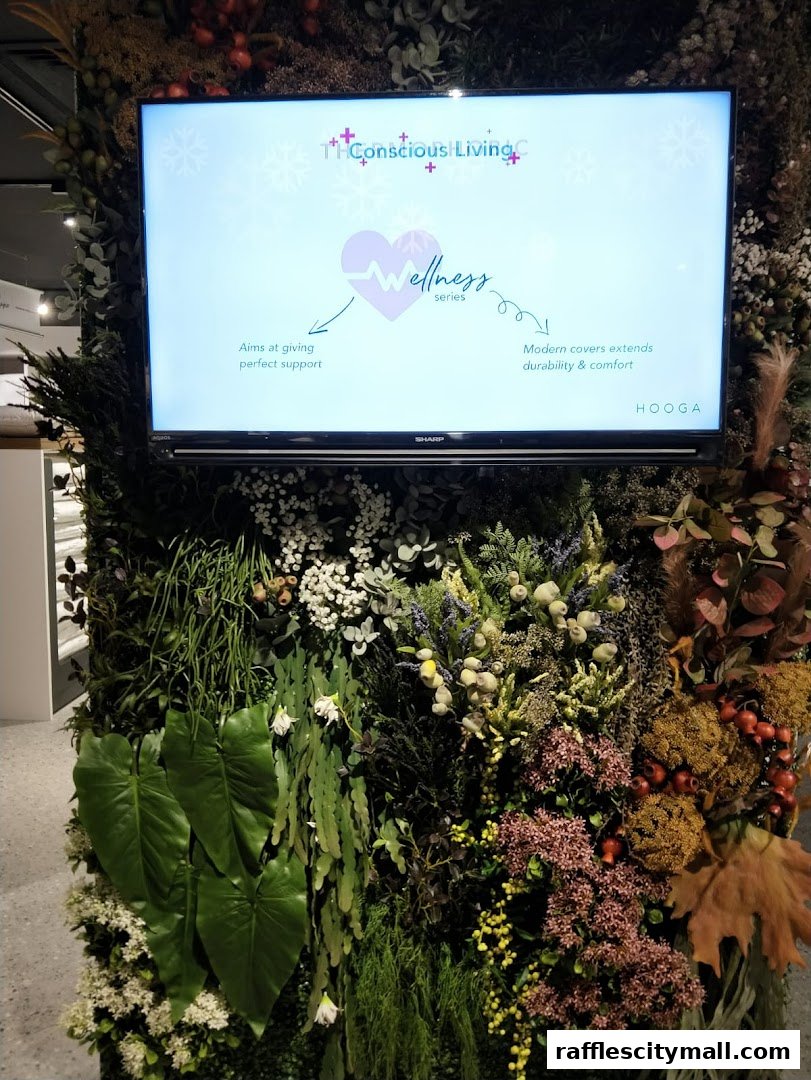 A screen displays information about HOOGA's Wellness series, surrounded by a lush green wall.