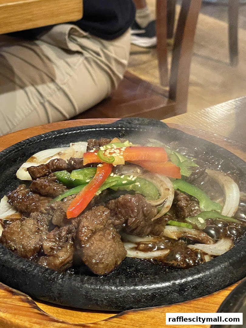 A sizzling hot plate of Korean bulgogi with vegetables and sesame seeds.