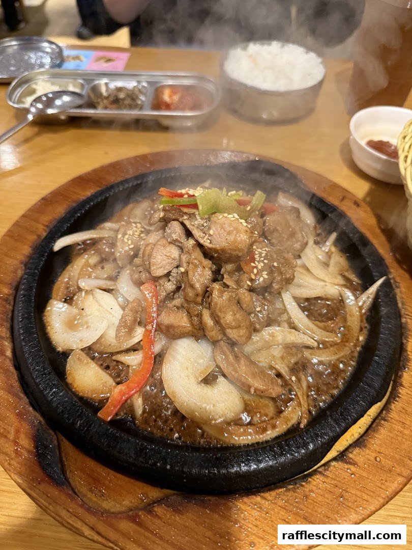 A sizzling Korean dish served on a hot plate with rice and side dishes.