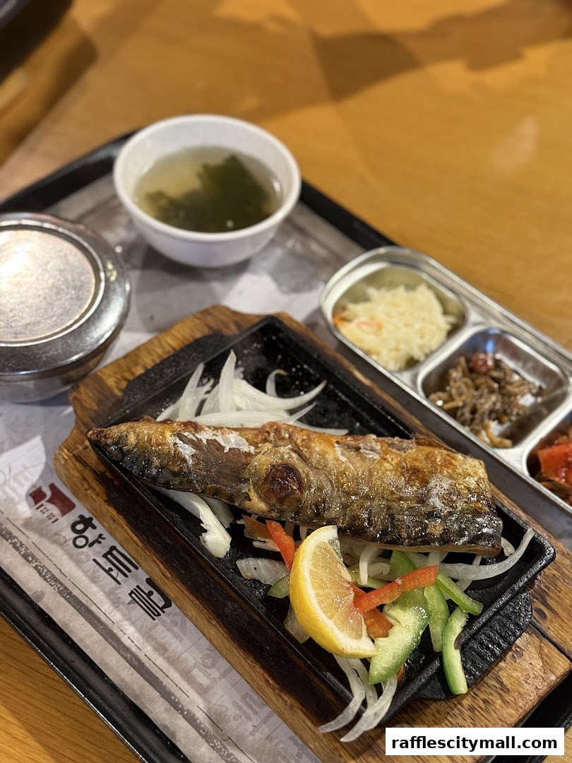 A grilled fish dish served with soup and side dishes on a tray.