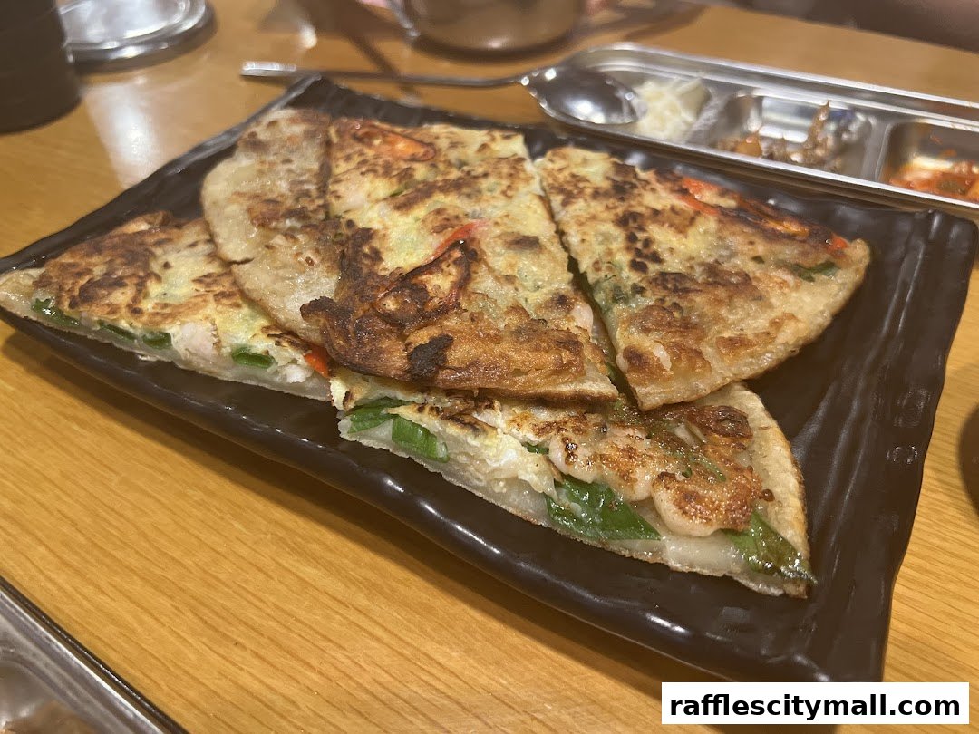 A close-up shot of a Korean pancake with seafood and vegetables on a black plate.