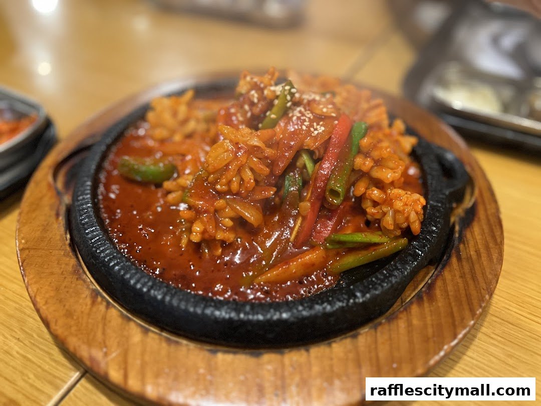 A close-up shot of a sizzling Korean dish with rice, vegetables, and sauce on a hot plate.