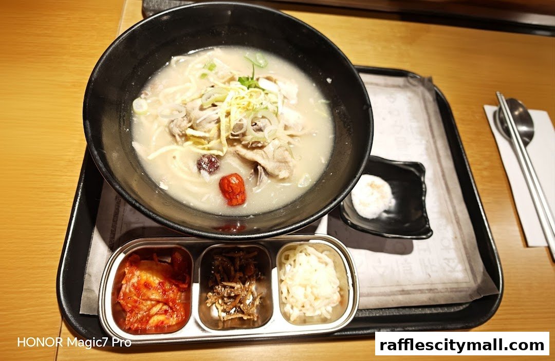 A bowl of Korean noodle soup with side dishes and chopsticks on a tray.