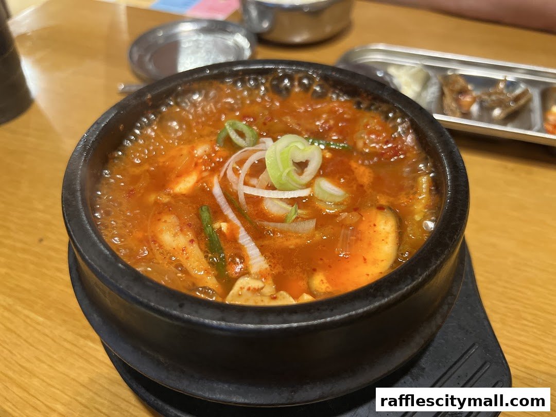 A close-up of a steaming bowl of Korean soft tofu stew with garnishes.