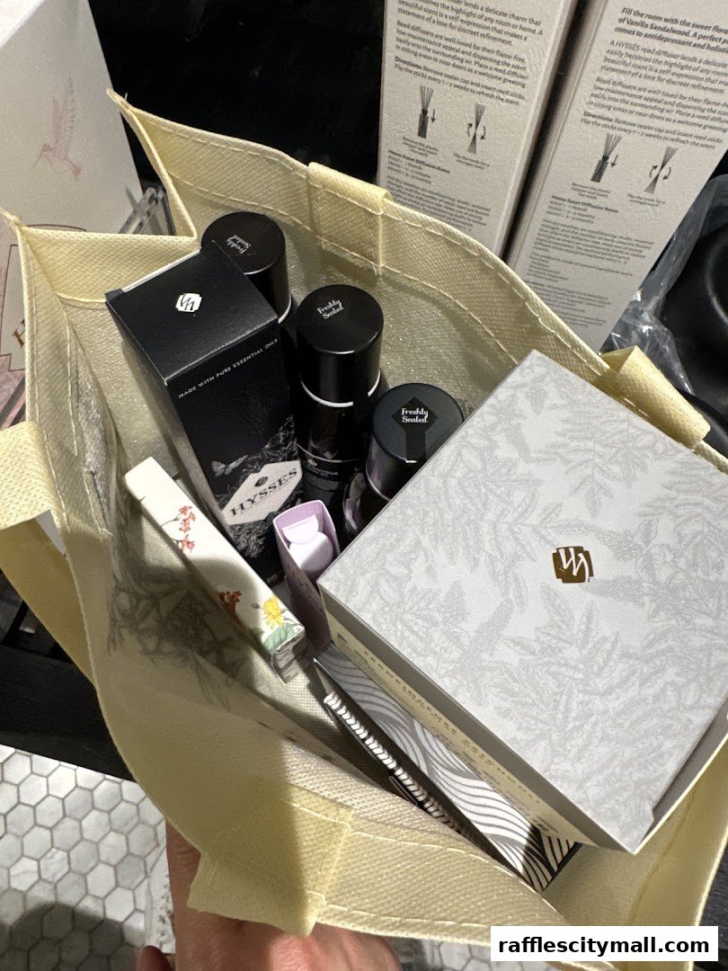 A person holds a reusable tote bag filled with HYSSES branded products, including essential oils and diffusers.