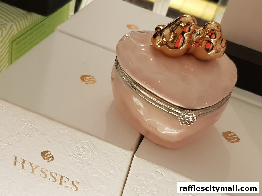 A pink heart-shaped trinket box with a gold bow sits on white boxes with the HYSSES logo.