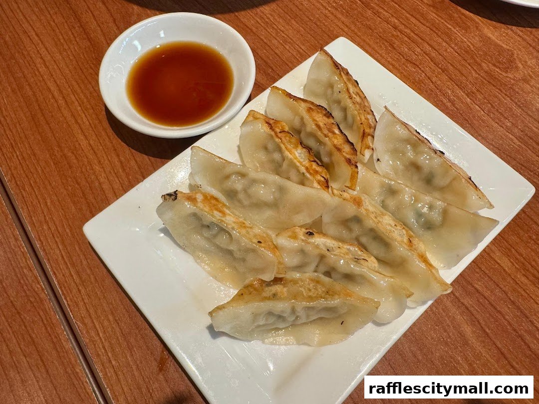 A plate of pan-fried gyoza dumplings with a side of dipping sauce.