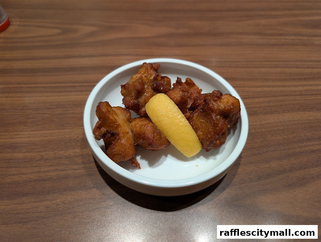 A white bowl filled with crispy fried chicken pieces and a lemon wedge on a wooden table.