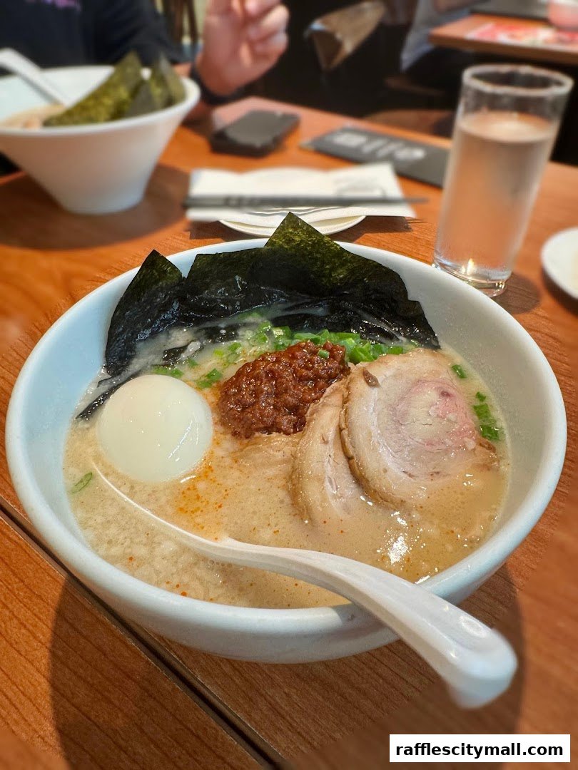 A close-up of a delicious bowl of ramen with pork, egg, nori, and chili paste.