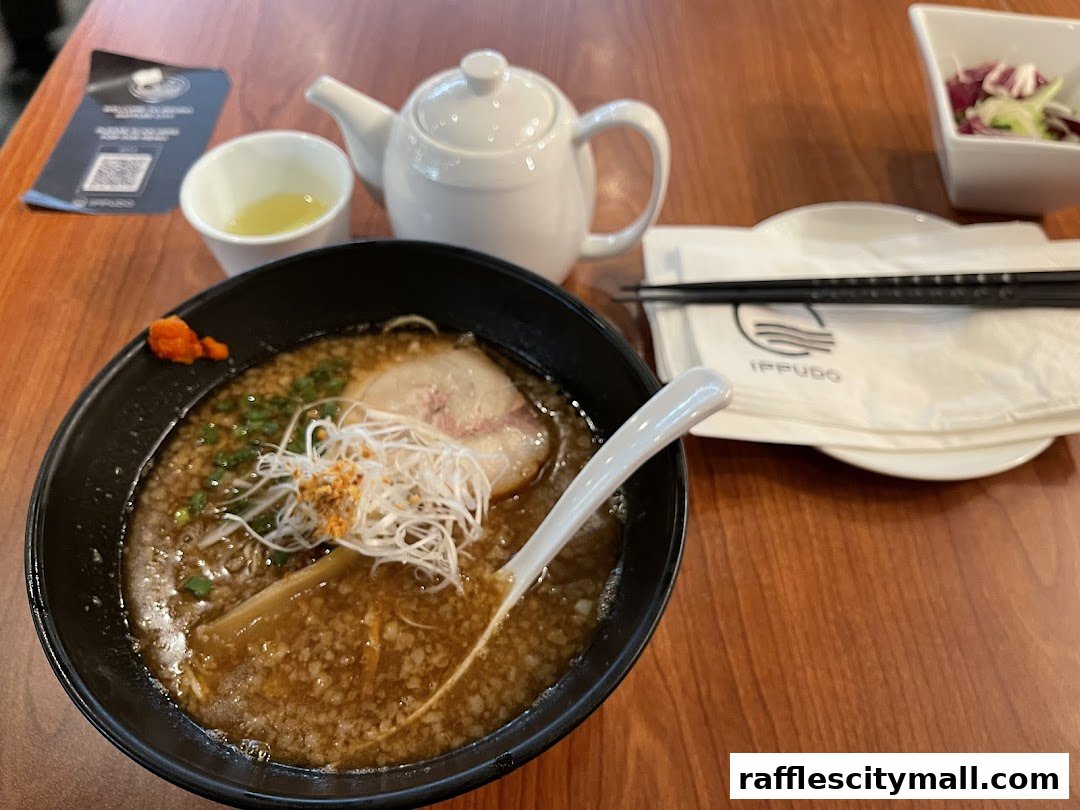 A steaming bowl of ramen with pork, noodles, and toppings, served with tea and chopsticks.