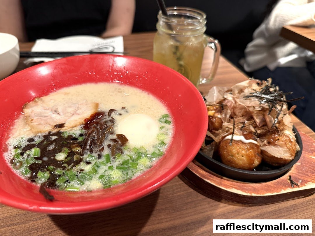 A bowl of ramen and takoyaki are served on a wooden table.