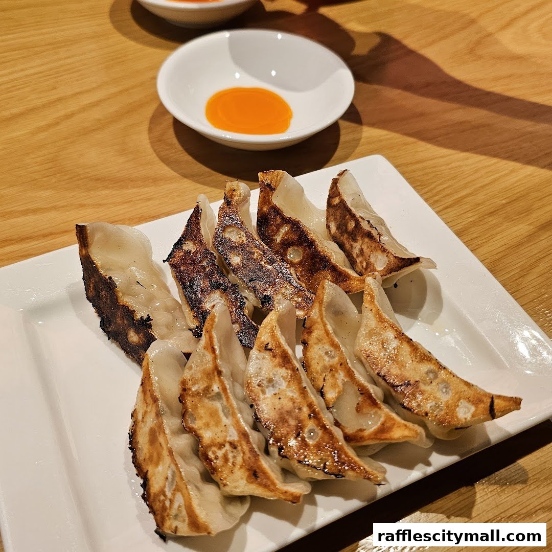 A plate of pan-fried gyoza dumplings with a dipping sauce on a wooden table.