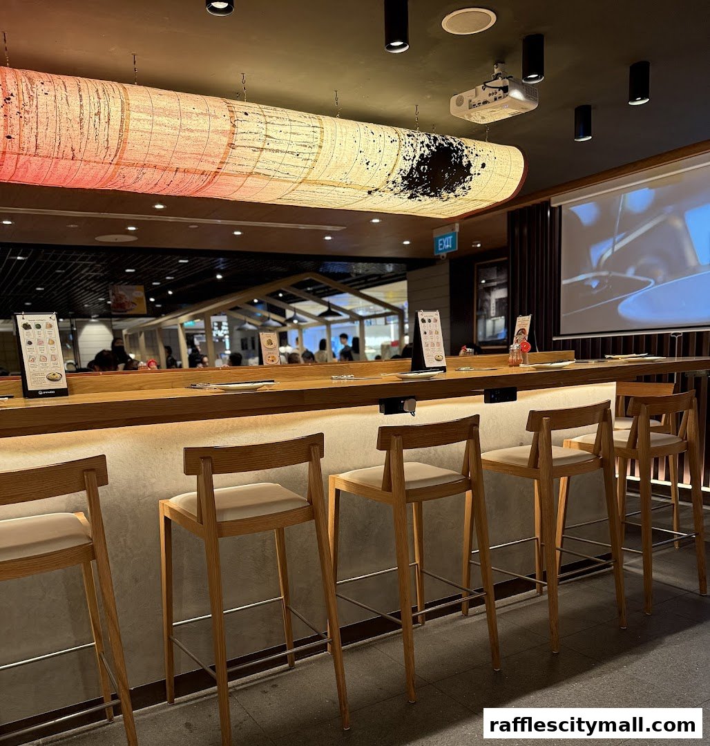 Interior shot of IPPUDO Raffles City showing a modern bar with wooden stools and a large decorative light.