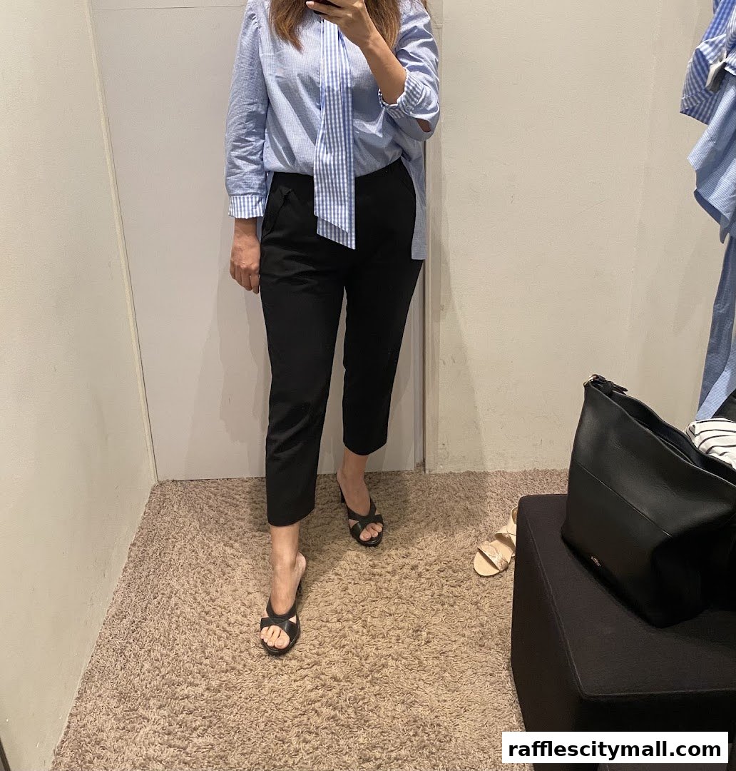 A person tries on a blue striped shirt and black pants in a fitting room.