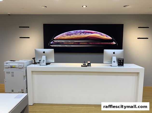 A clean, modern retail counter with Apple computers and a large iPhone advertisement.