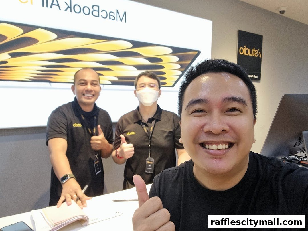 Three smiling men in iStudio shirts give thumbs up in front of a MacBook Air display.