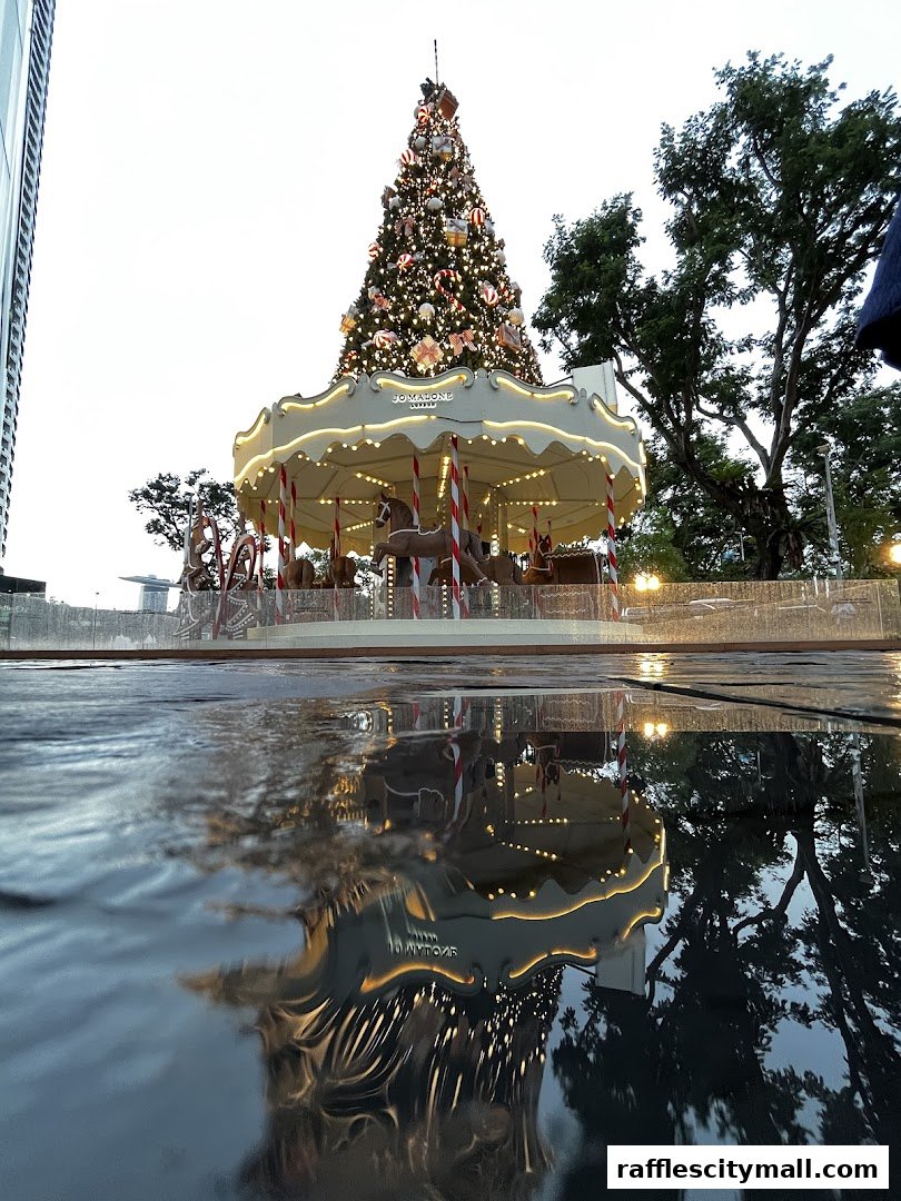 A festive carousel and Christmas tree reflected in wet pavement.