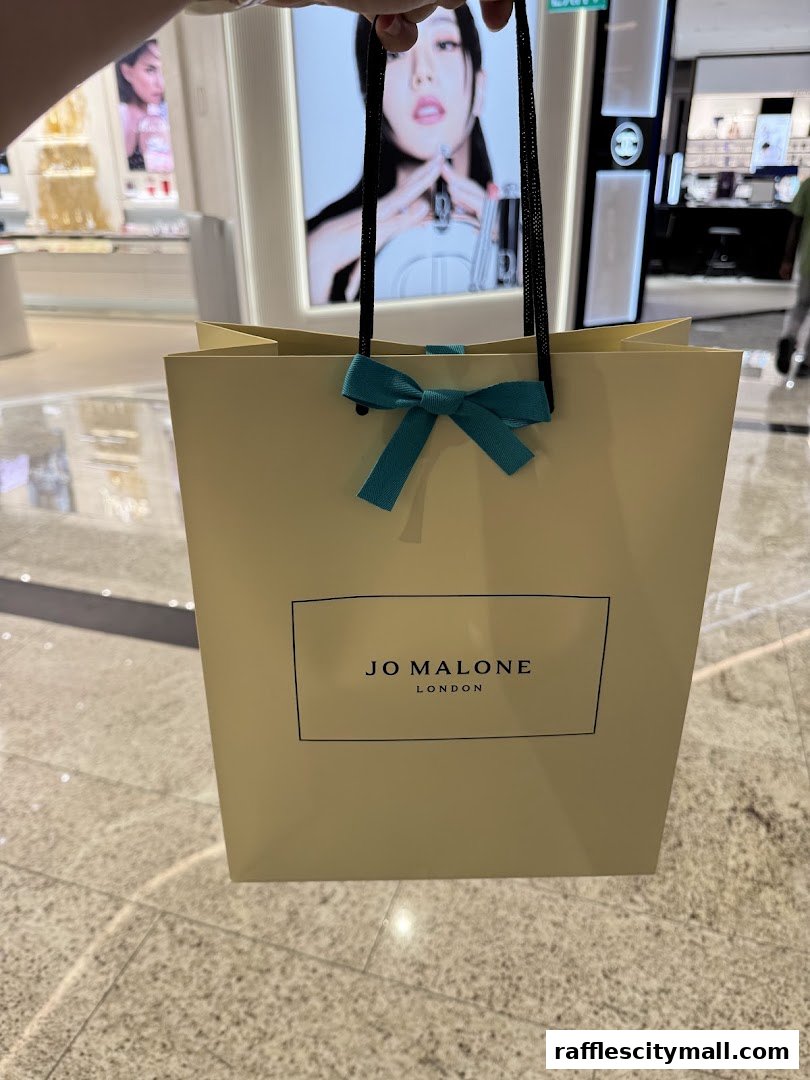 A person holds a Jo Malone London shopping bag in front of a store display.