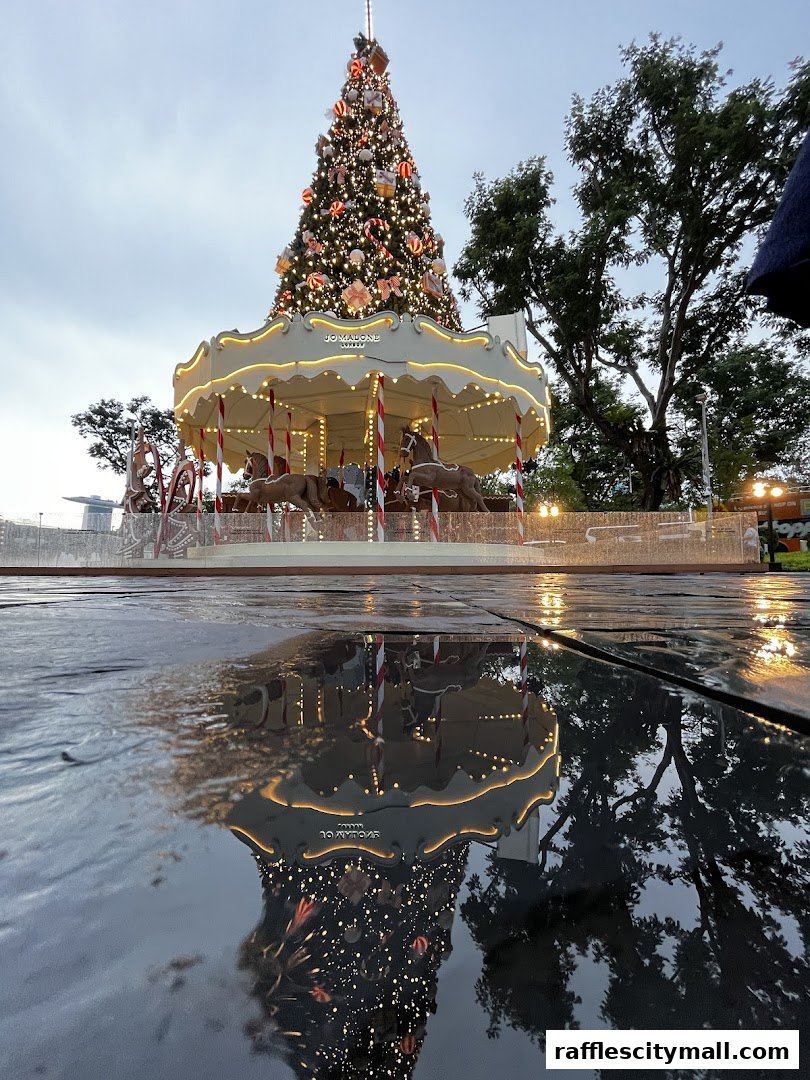 A festive Christmas tree and carousel with Jo Malone branding, reflected in wet pavement.