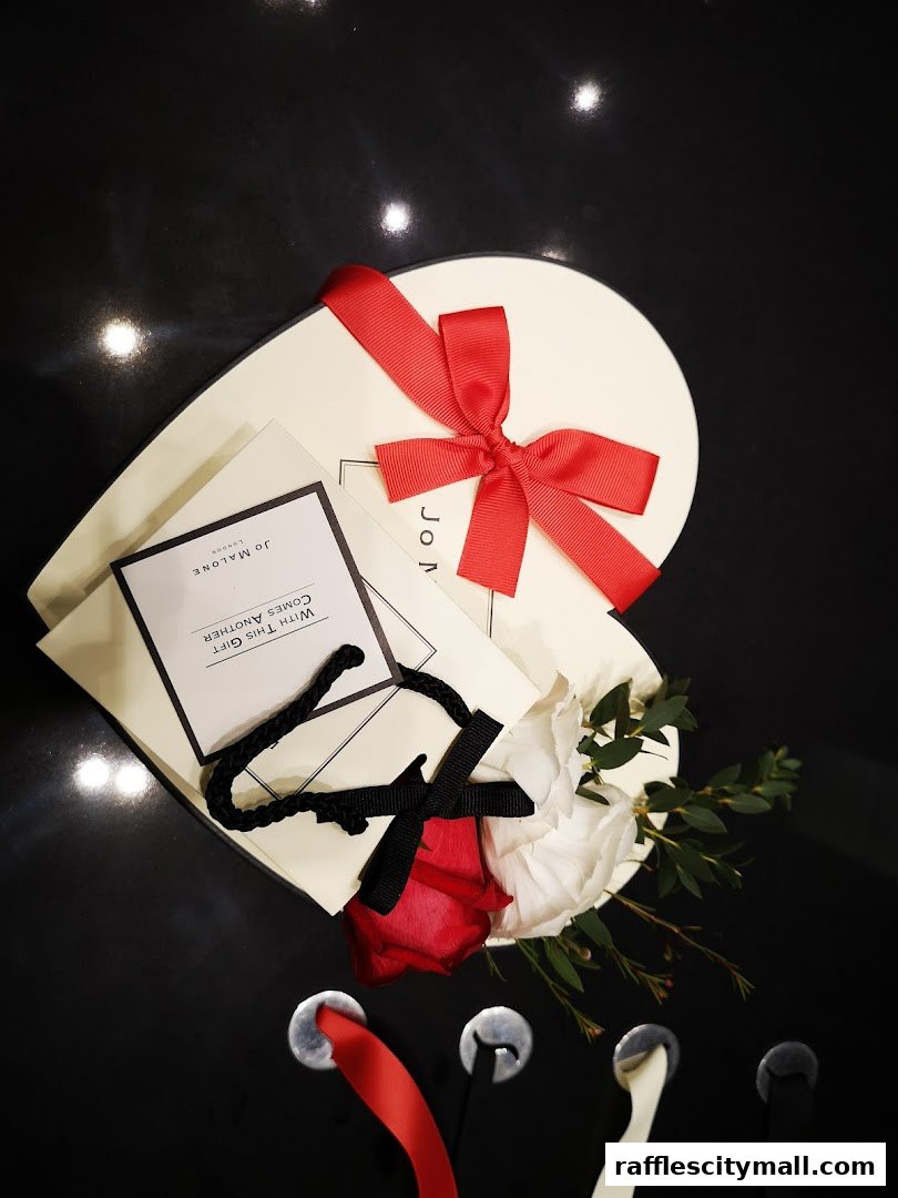A Jo Malone London gift box with red ribbon, flowers, and a shopping bag.