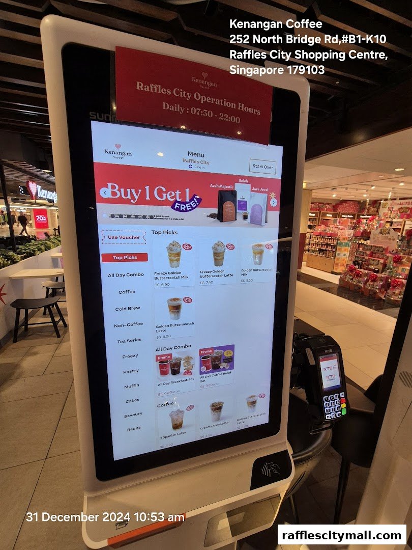 A digital menu screen at Kenangan Coffee Raffles City, displaying promotions and coffee items.