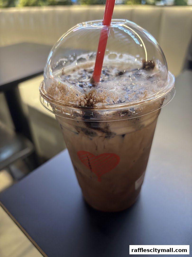 A close-up of an iced coffee drink with a red straw and a heart logo on the cup.