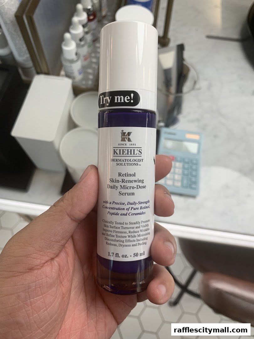 A hand holds a Kiehl's Retinol Skin-Renewing Daily Micro-Dose Serum bottle.