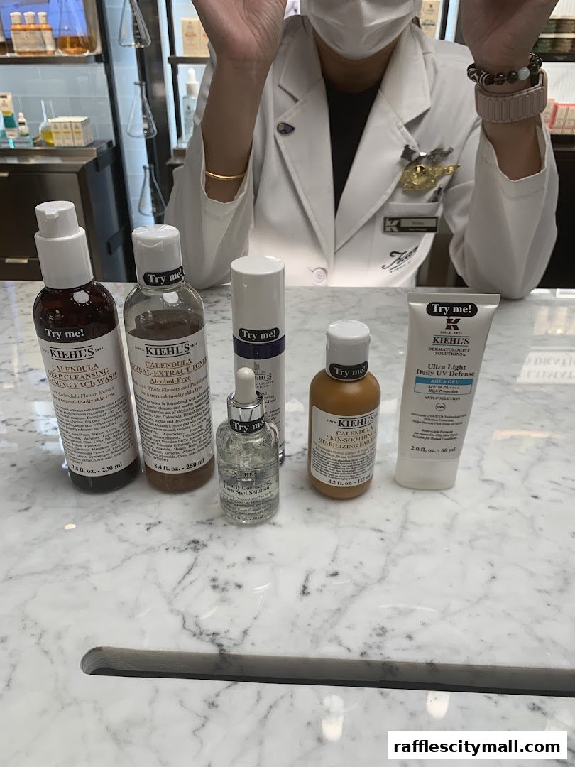 A collection of Kiehl's skincare products displayed on a marble counter with a staff member in the background.